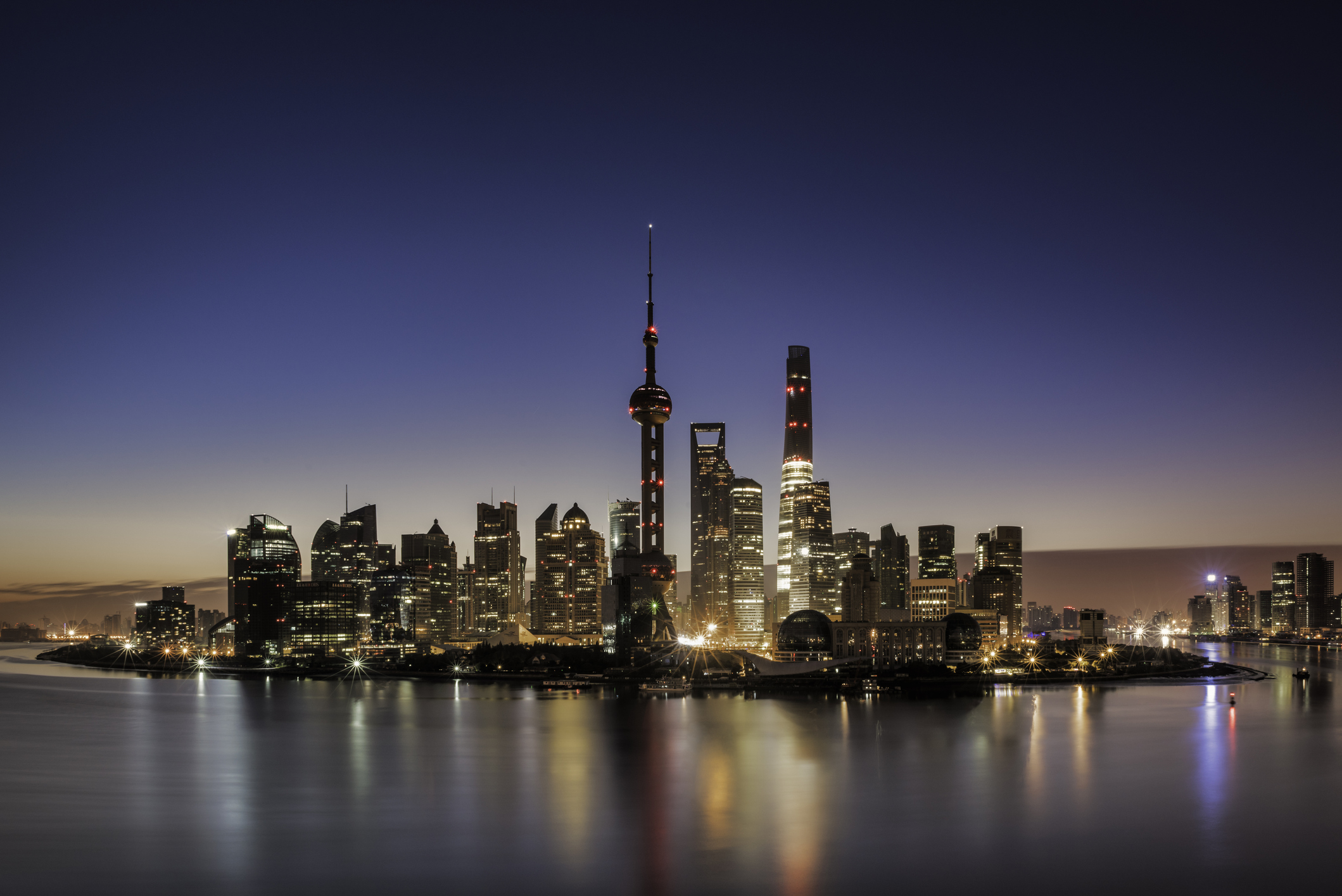 Shanghai Bund at night — the Pudong skyline in deep blue illumination reflected across the Huangpu River